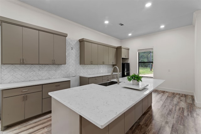 kitchen featuring gray cabinetry, sink, wood-type flooring, a center island with sink, and ornamental molding