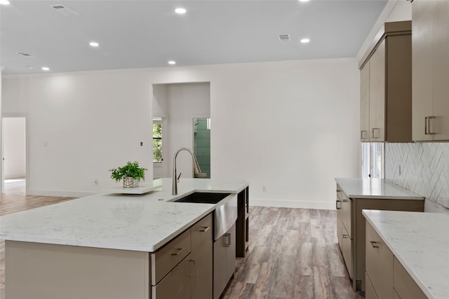 kitchen featuring sink, tasteful backsplash, a large island, light hardwood / wood-style floors, and light stone counters