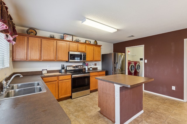 kitchen featuring separate washer and dryer, appliances with stainless steel finishes, a textured ceiling, sink, and a center island