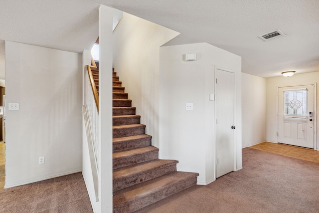 stairway with carpet floors and a textured ceiling