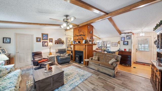 living area with lofted ceiling with beams, a textured ceiling, a ceiling fan, and a fireplace