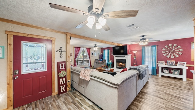 living area featuring a textured ceiling, a ceiling fan, wood finished floors, and a warm lit fireplace