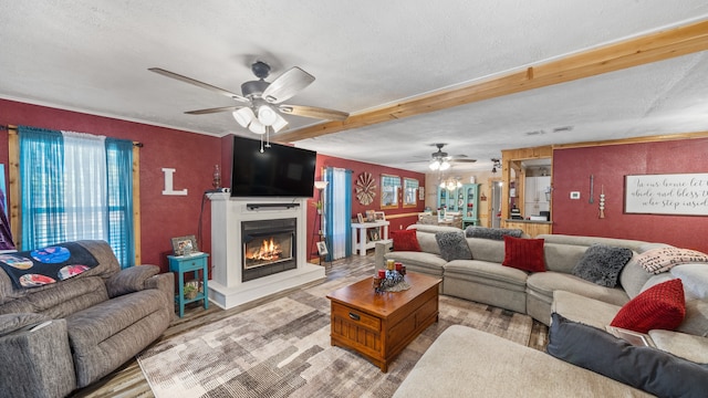 living area with a textured ceiling, light wood-style flooring, beam ceiling, a glass covered fireplace, and a ceiling fan