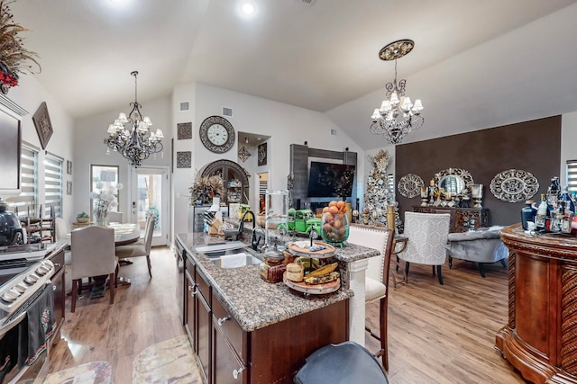 kitchen featuring light wood-type flooring, decorative light fixtures, light stone countertops, sink, and lofted ceiling