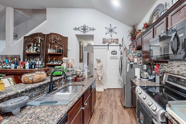 kitchen featuring stainless steel appliances, light hardwood / wood-style floors, sink, a barn door, and vaulted ceiling