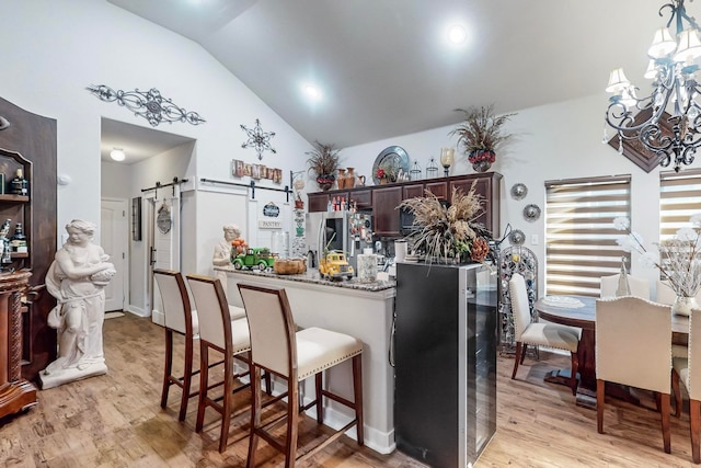 kitchen featuring vaulted ceiling, kitchen peninsula, a barn door, stainless steel refrigerator, and light hardwood / wood-style flooring