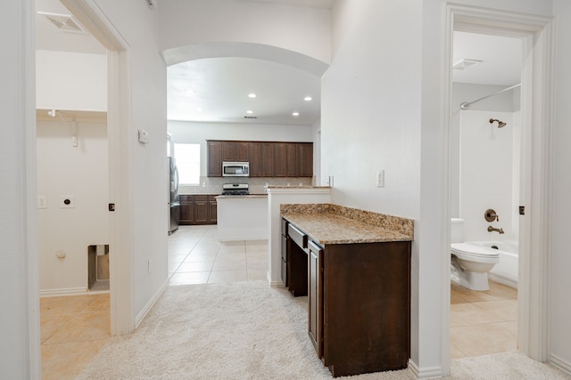 kitchen featuring light stone countertops, dark brown cabinets, stainless steel appliances, and light tile patterned flooring