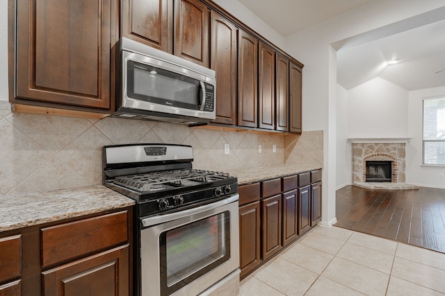 kitchen featuring a fireplace, appliances with stainless steel finishes, light wood-type flooring, and light stone countertops