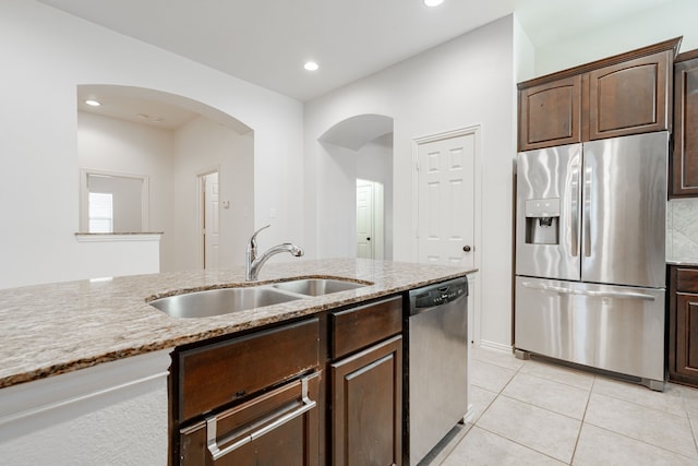 kitchen with light stone countertops, dark brown cabinets, stainless steel appliances, sink, and light tile patterned floors