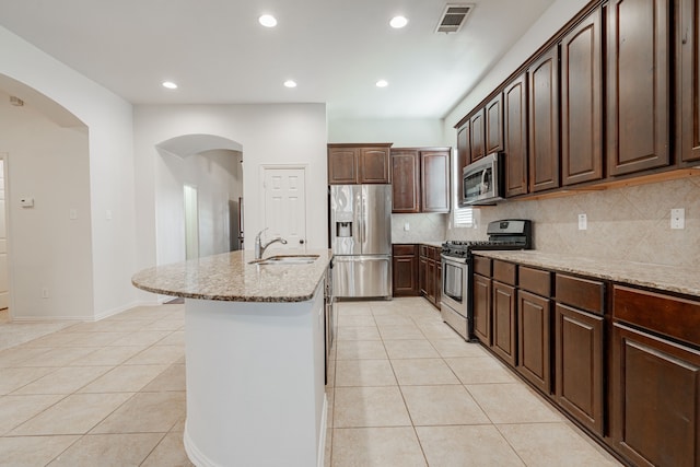 kitchen with dark brown cabinets, light tile patterned flooring, an island with sink, and appliances with stainless steel finishes