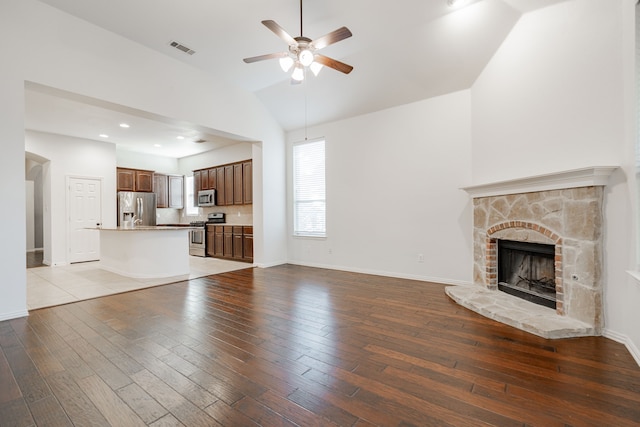 unfurnished living room featuring a stone fireplace, ceiling fan, light hardwood / wood-style flooring, and vaulted ceiling