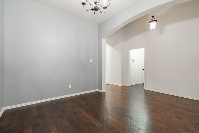 spare room featuring baseboards, a chandelier, and dark wood-style flooring