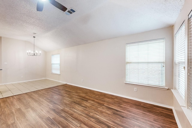 empty room featuring a textured ceiling, lofted ceiling, ceiling fan with notable chandelier, and hardwood / wood-style flooring