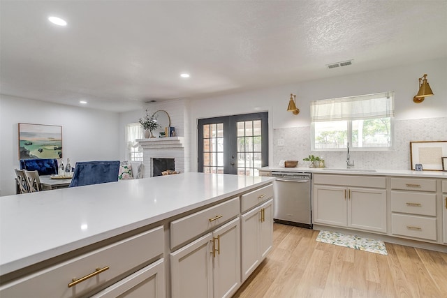 kitchen featuring light hardwood / wood-style floors, plenty of natural light, stainless steel dishwasher, and a fireplace