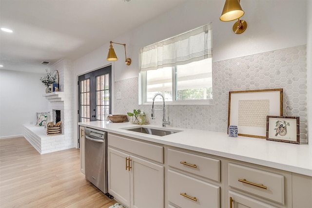 kitchen featuring light hardwood / wood-style floors, dishwasher, hanging light fixtures, sink, and a fireplace