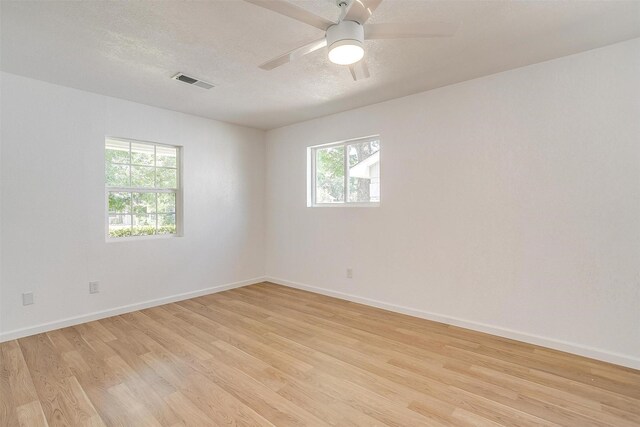 spare room featuring a textured ceiling, a wealth of natural light, light hardwood / wood-style floors, and ceiling fan