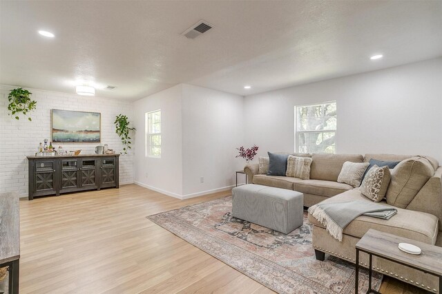 living room featuring a wealth of natural light, a textured ceiling, light hardwood / wood-style floors, and brick wall