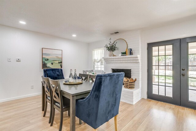 dining room with french doors, a fireplace, and light wood-type flooring