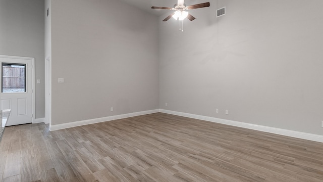 empty room featuring ceiling fan, light hardwood / wood-style flooring, and a towering ceiling