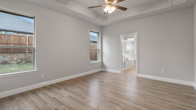 empty room featuring ceiling fan, light hardwood / wood-style floors, and a tray ceiling