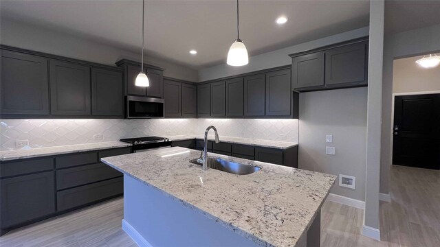 kitchen with a center island with sink, sink, appliances with stainless steel finishes, white cabinets, and light stone counters