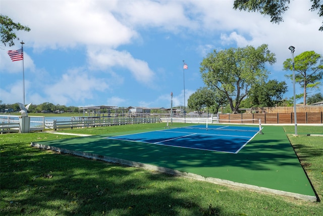 view of tennis court with a lawn and a water view