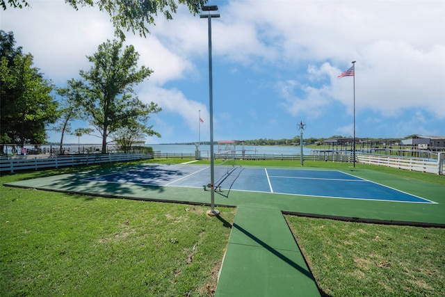 view of tennis court featuring a water view and a lawn