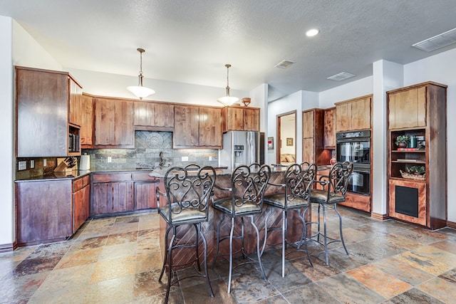 1133 Brackeen Dr, Graford, TX 76449 - kitchen with stainless steel appliances, stone tile flooring, a breakfast bar area, dark countertops, and a textured ceiling