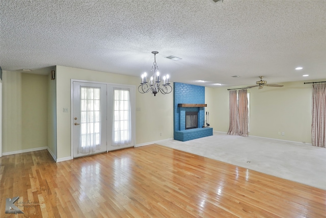 unfurnished living room with light wood-type flooring, a textured ceiling, ceiling fan with notable chandelier, and a brick fireplace