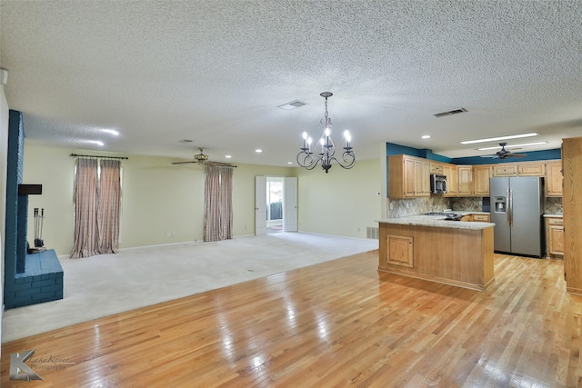 kitchen with hanging light fixtures, kitchen peninsula, light hardwood / wood-style floors, decorative backsplash, and appliances with stainless steel finishes