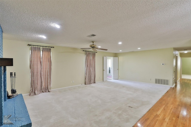 unfurnished living room featuring a textured ceiling, light colored carpet, and ceiling fan