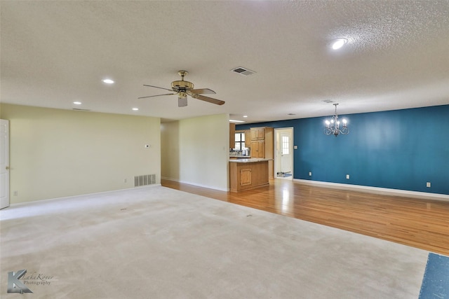 unfurnished living room with ceiling fan with notable chandelier, a textured ceiling, and light hardwood / wood-style floors