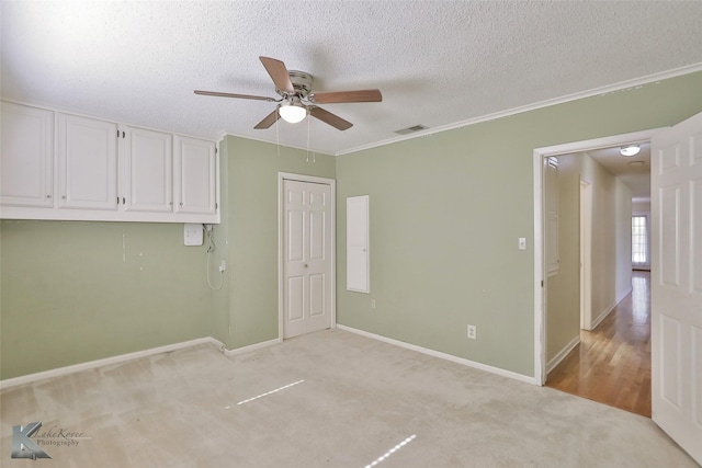 carpeted spare room with ceiling fan, crown molding, and a textured ceiling