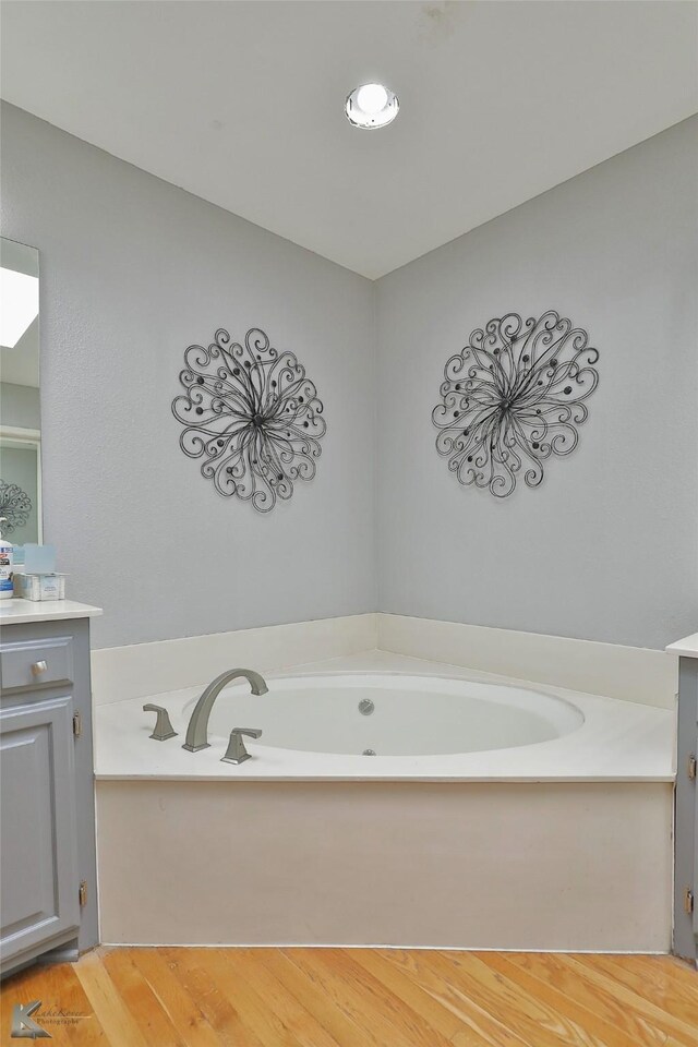 bathroom with a tub to relax in, vanity, and wood-type flooring