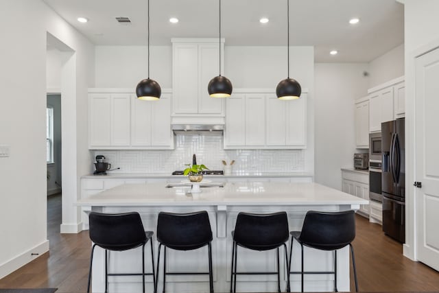 kitchen featuring appliances with stainless steel finishes, white cabinetry, a kitchen island with sink, and hanging light fixtures