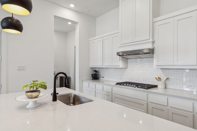 kitchen with decorative backsplash, wall chimney exhaust hood, stainless steel gas cooktop, sink, and white cabinetry