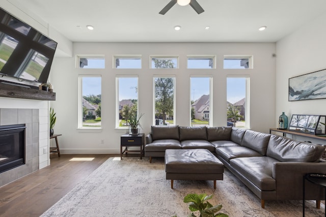 living room with wood-type flooring, ceiling fan, a wealth of natural light, and a tiled fireplace