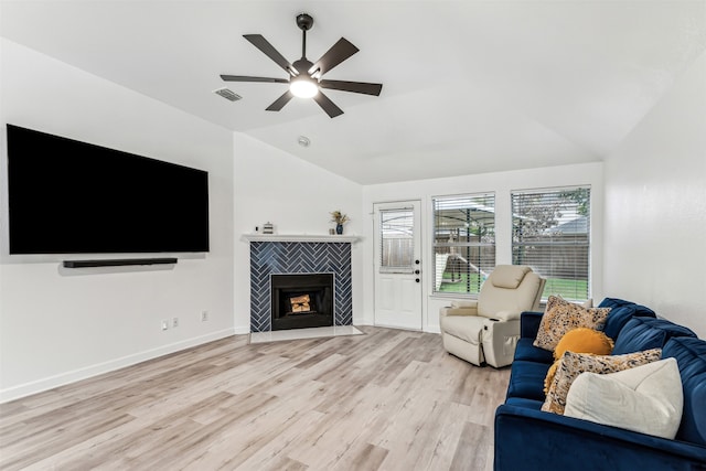 living room featuring light wood-type flooring, ceiling fan, lofted ceiling, and a tiled fireplace