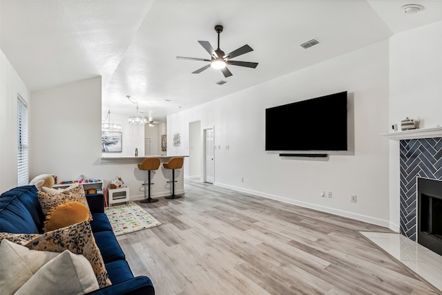 living room with ceiling fan with notable chandelier, light hardwood / wood-style floors, and a tiled fireplace