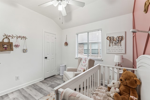 bedroom featuring a crib, light wood-type flooring, ceiling fan, and lofted ceiling