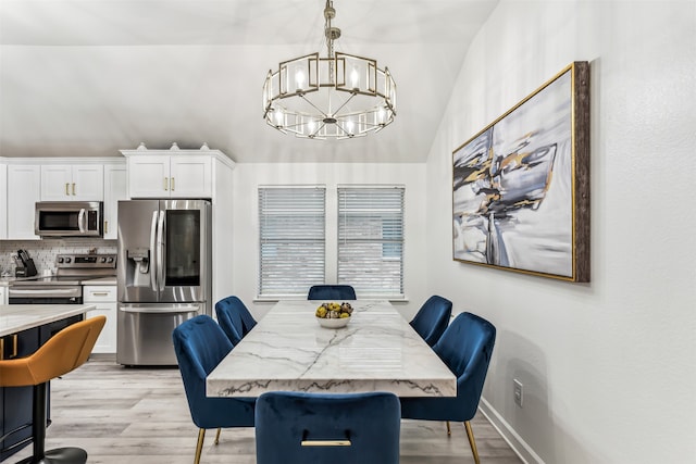 dining area with vaulted ceiling, an inviting chandelier, and light hardwood / wood-style flooring