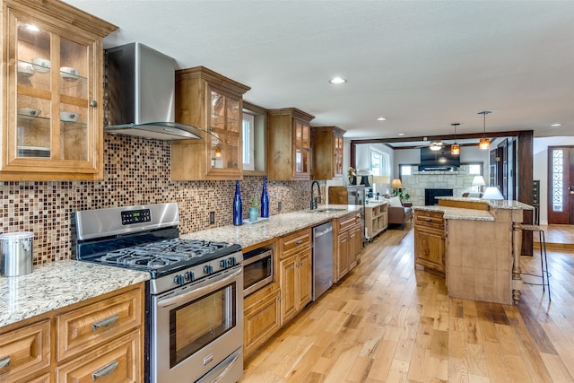 kitchen featuring sink, wall chimney range hood, a breakfast bar, light wood-type flooring, and appliances with stainless steel finishes