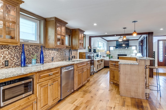 kitchen featuring appliances with stainless steel finishes, light stone countertops, sink, light hardwood / wood-style floors, and a breakfast bar area