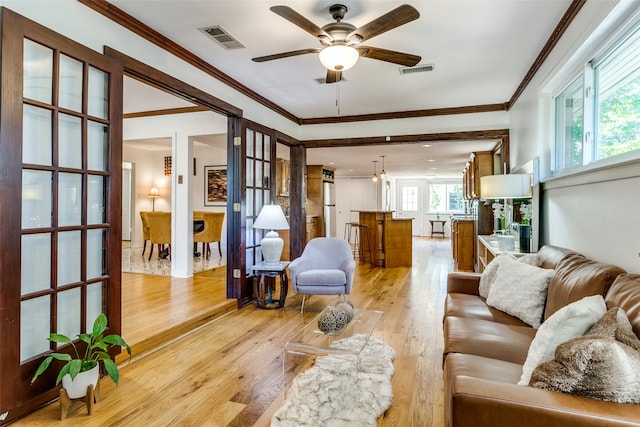 living room with ceiling fan with notable chandelier, ornamental molding, and light hardwood / wood-style flooring