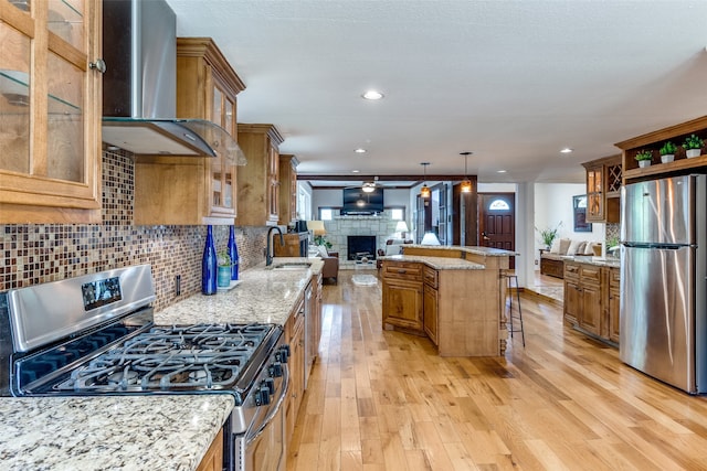 kitchen featuring stainless steel appliances, light hardwood / wood-style floors, wall chimney range hood, a breakfast bar, and light stone countertops