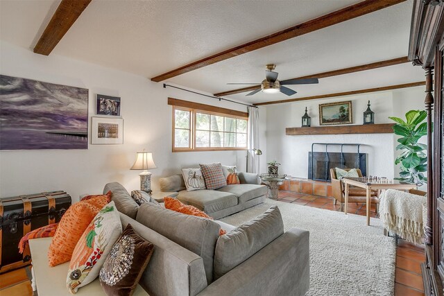 living room featuring a textured ceiling, a fireplace, ceiling fan, and beam ceiling