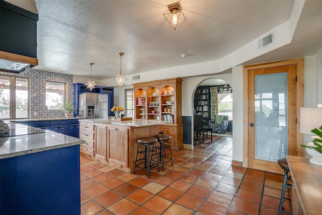 kitchen featuring a textured ceiling, a healthy amount of sunlight, a center island, and stainless steel fridge