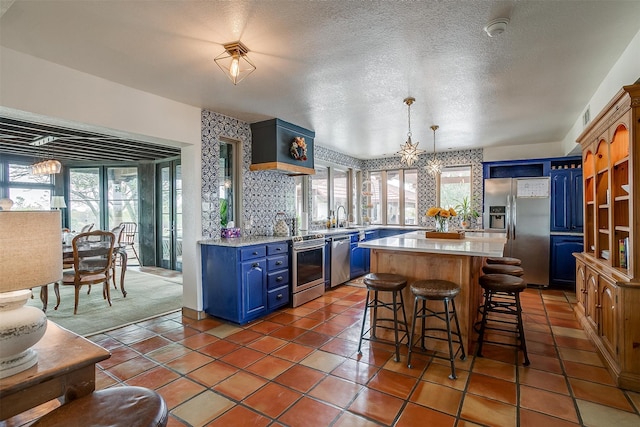 kitchen with sink, appliances with stainless steel finishes, a textured ceiling, a center island, and blue cabinets