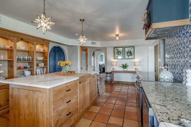 kitchen featuring a textured ceiling, a kitchen island, ventilation hood, stainless steel electric stove, and pendant lighting