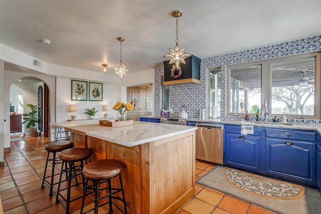 kitchen featuring a kitchen breakfast bar, a textured ceiling, stainless steel dishwasher, a kitchen island, and blue cabinets